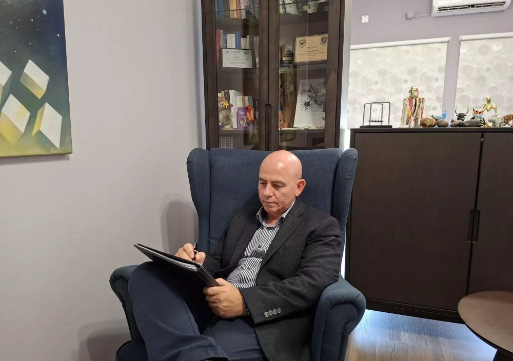 Ο Δρ. Νίκος Ηλία κρατά σημειώσεις σε μια πολυθρόνα στον χώρο θεραπείας του γραφείου του